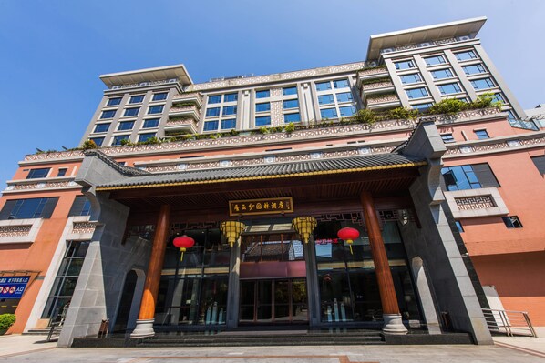 A multi-story hotel with a traditional architectural style, featuring a prominent entrance with a tiled roof and two red lanterns.