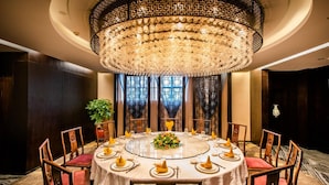 A round dining table with a floral centerpiece, surrounded by wooden chairs with red cushions. - Xiang Yun Sha Garden Hotel (Foshan)