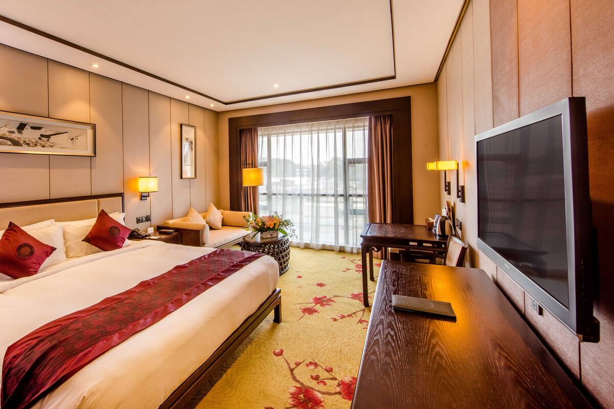 Une chambre d’hôtel avec un grand lit, une télévision, un bureau et une fenêtre avec des rideaux.