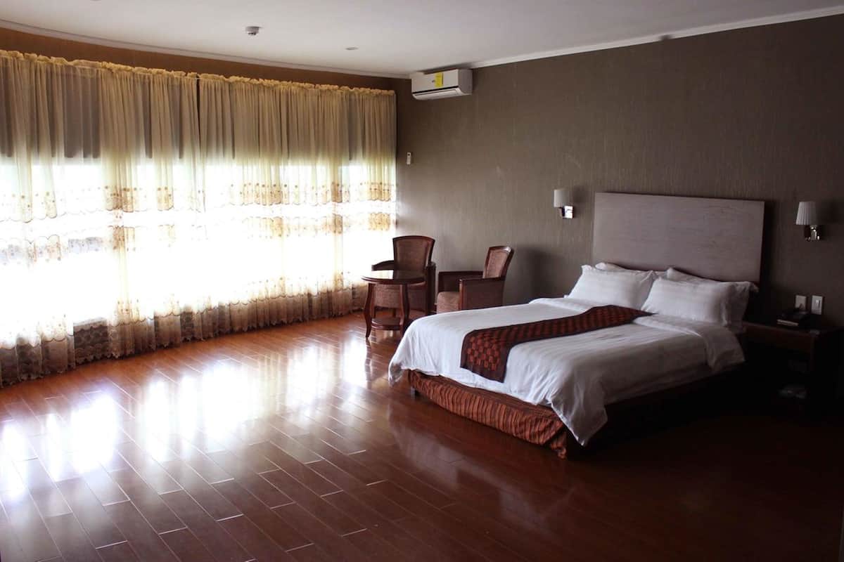 A hotel room with a large bed, a chair, a desk, and a window with curtains.