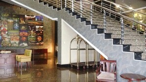 Un vestíbulo con una escalera de mármol, una zona de estar con una silla y una mesa, y una pared con un mosaico de imágenes.