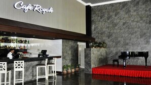 Zona de bar con un piano sobre un escenario rojo, un barman y una barra con botellas.