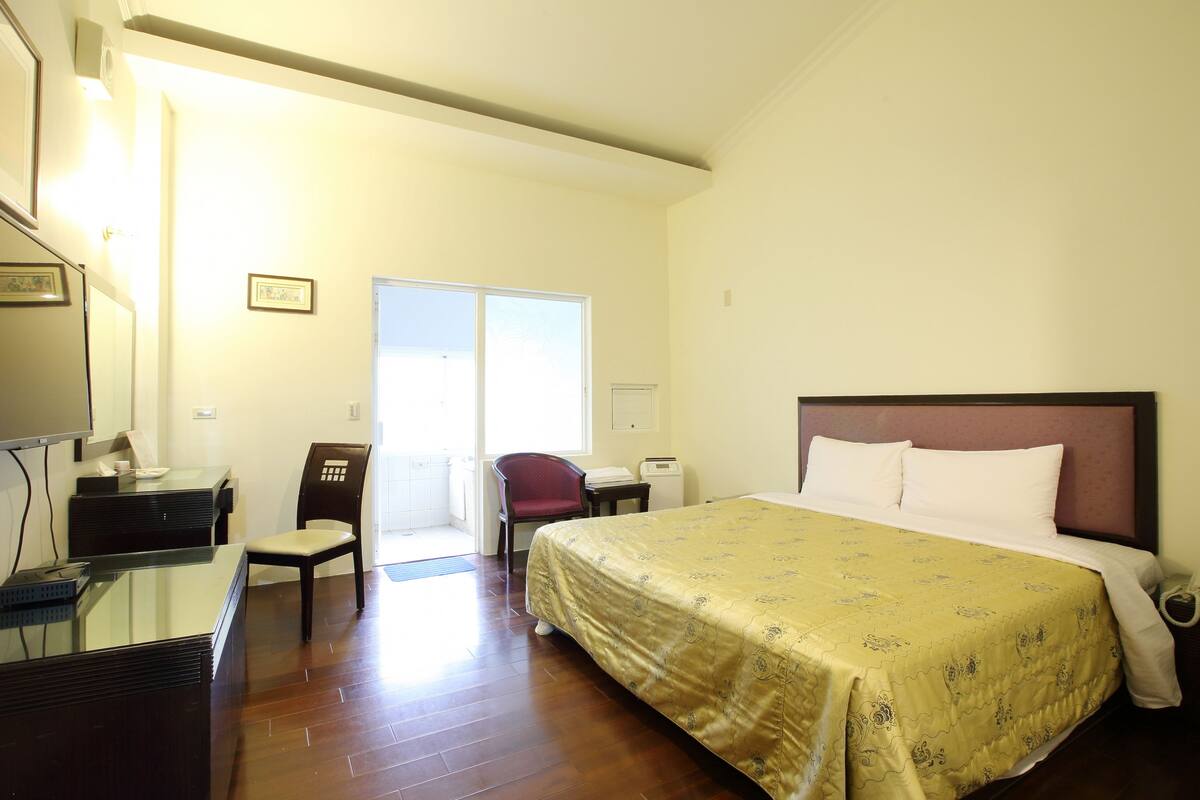 A hotel room with a bed, a desk, a chair, and a view of the outside.