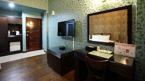 A hotel room with a wooden door, a television mounted on the wall, a desk with a chair, and a patterned wallpaper. - Cyuan Tang Hot Spring Hotel (Jiaoxi)