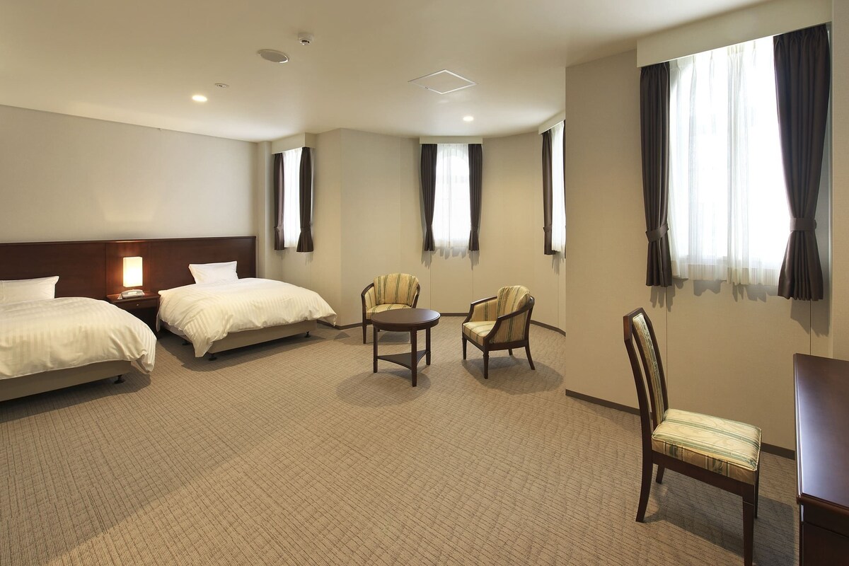 A hotel room with two beds, a small table, two chairs, and a desk.