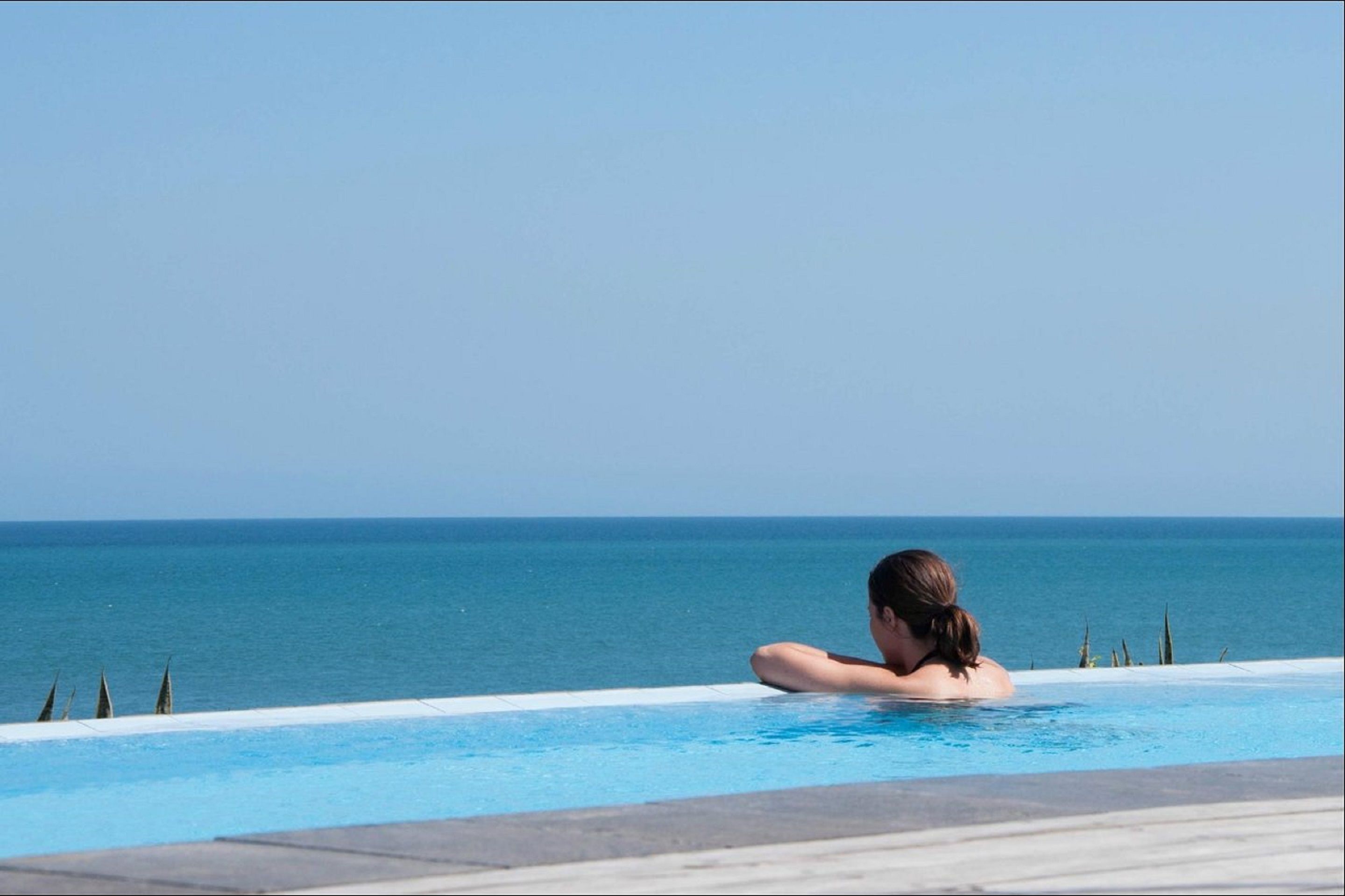 A person relaxing in a clear blue infinity pool with a view of the ocean.