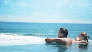 A couple relaxing in a clear blue infinity pool with a view of the ocean. - PNB Beach Resort (Pererenan)
