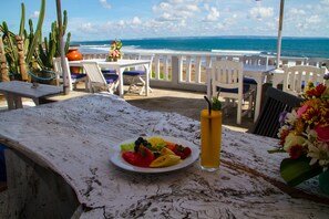A table with a plate of fruit and a drink, overlooking the ocean. - PNB Beach Resort (Pererenan)