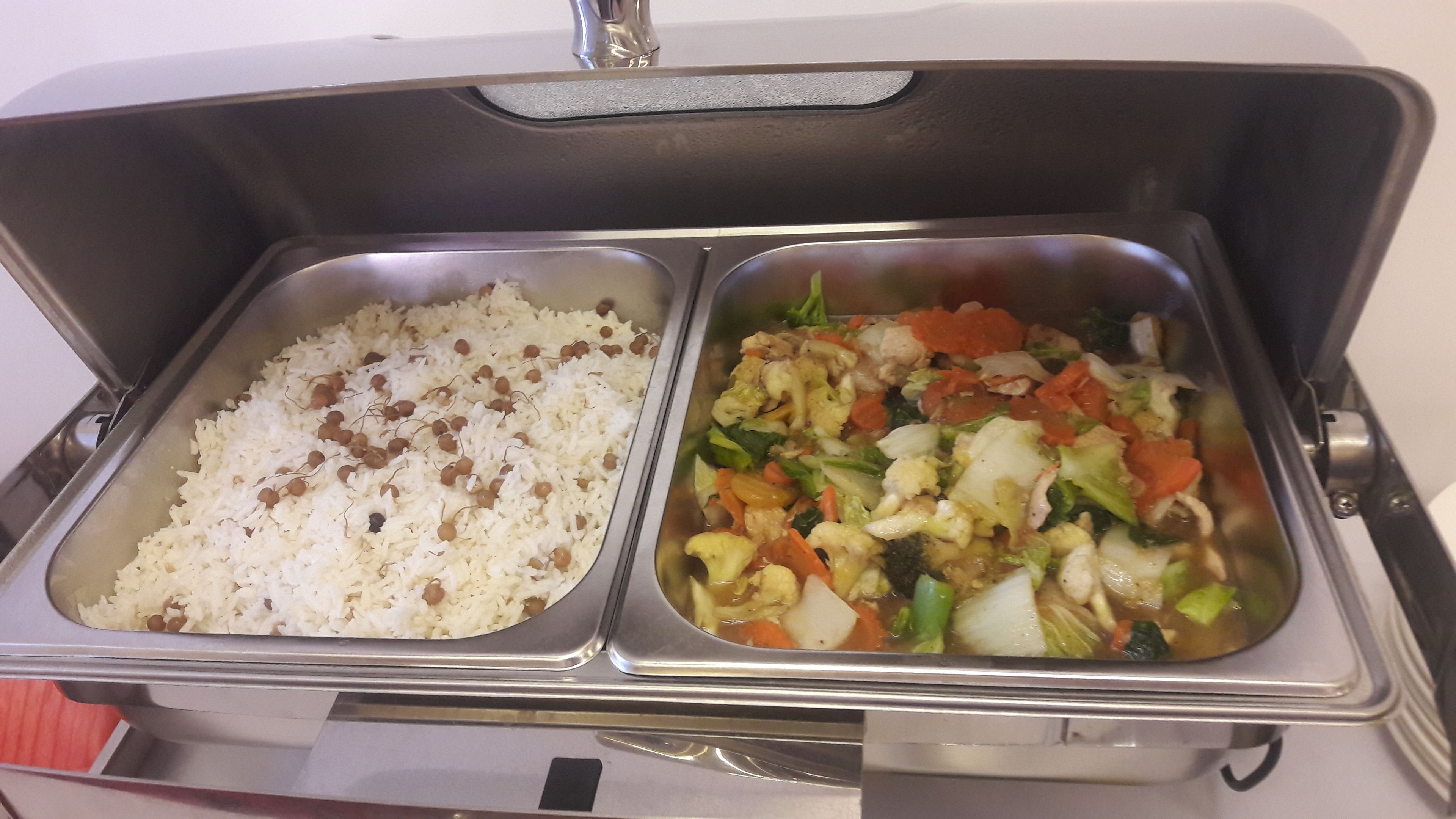 A buffet with two trays: one with rice and lentils, the other with mixed vegetables and chicken.