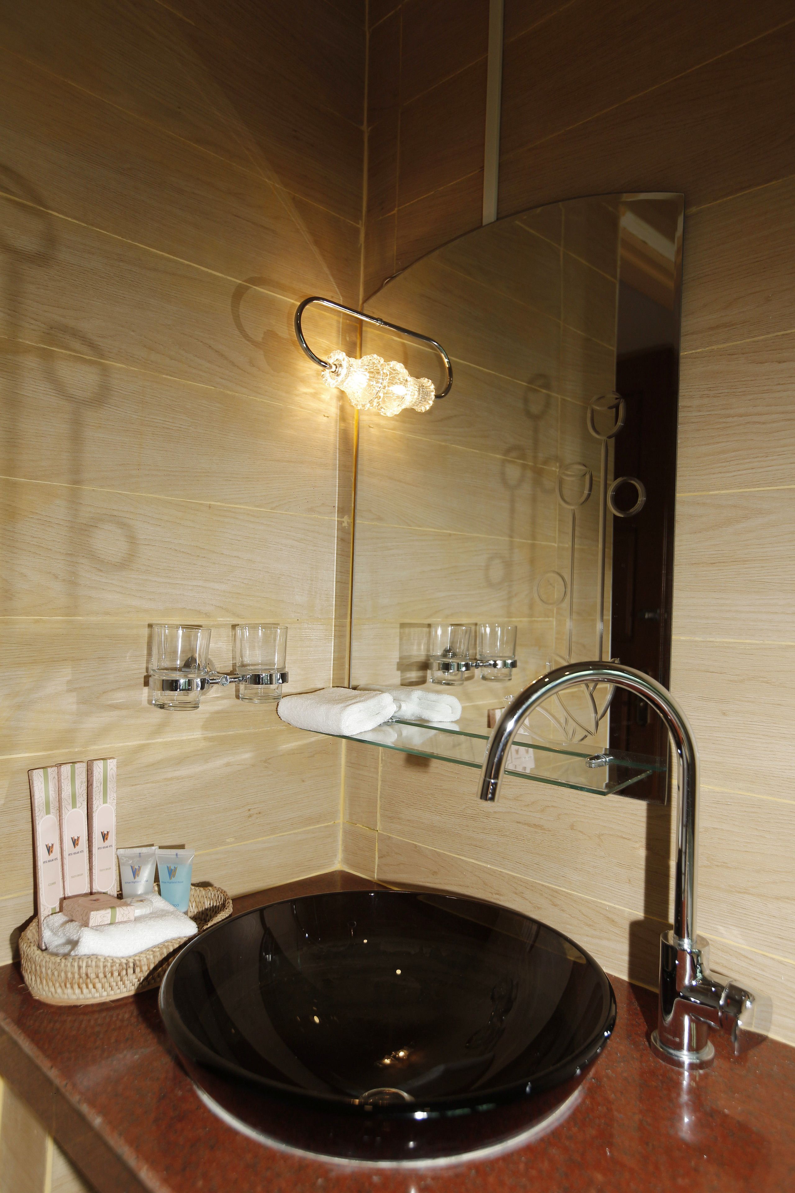 A bathroom with a black glass sink, a chrome faucet, and a mirror above it. There are two small glasses and a towel on the sink's edge.