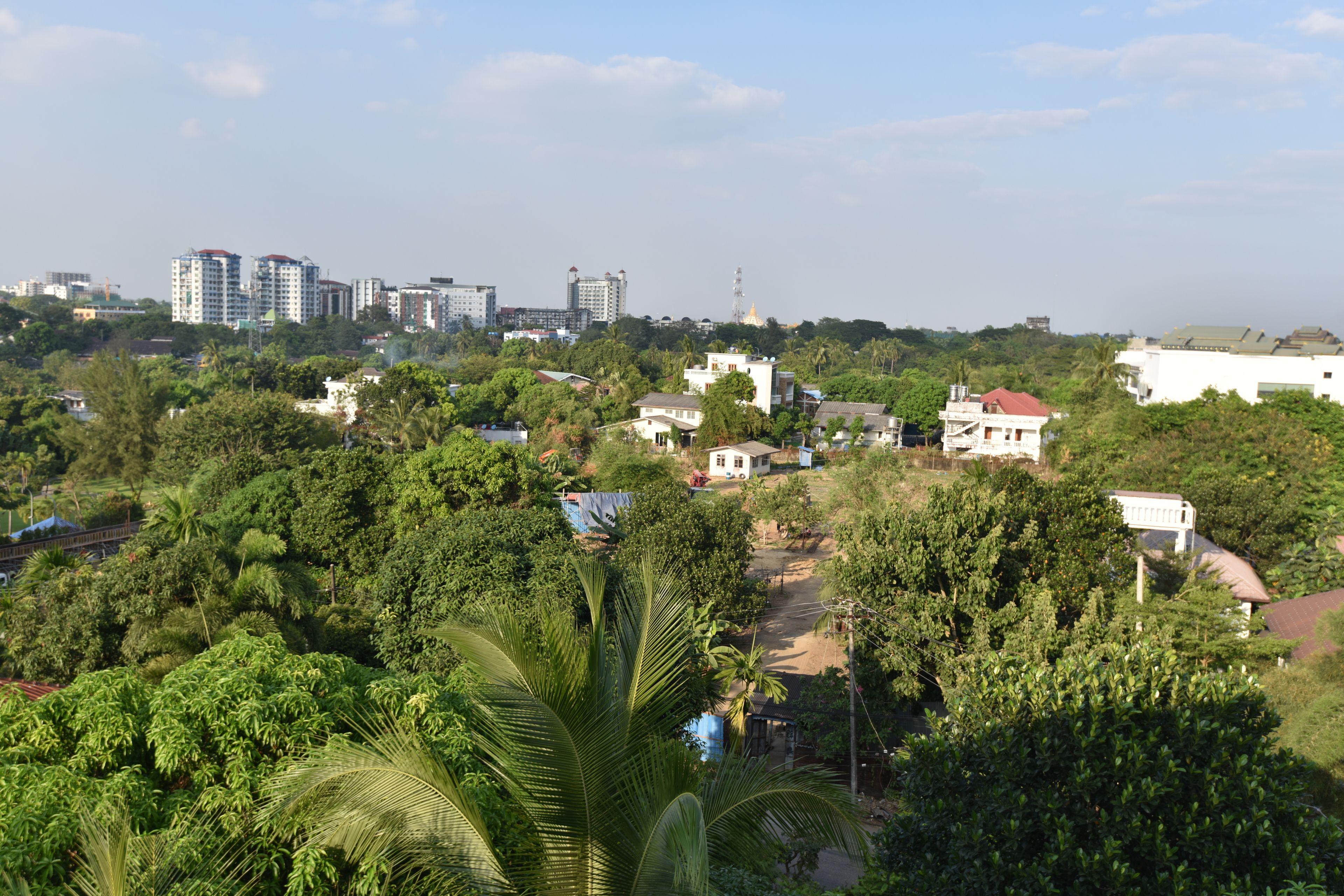 Una zona residencial con varios edificios, incluyendo una casa blanca destacada con techo rojo, rodeada de exuberante vegetación y palmeras.