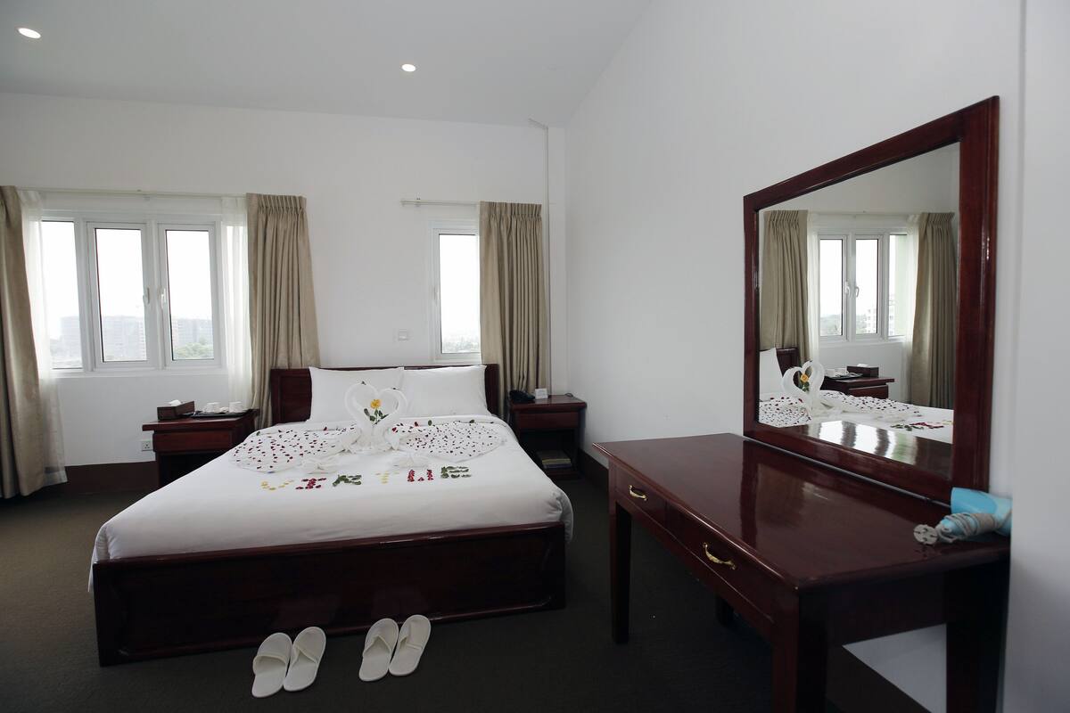 Habitación de hotel con una cama grande, una mesita de noche de madera, un aparador, un espejo y un par de zapatos en el suelo.