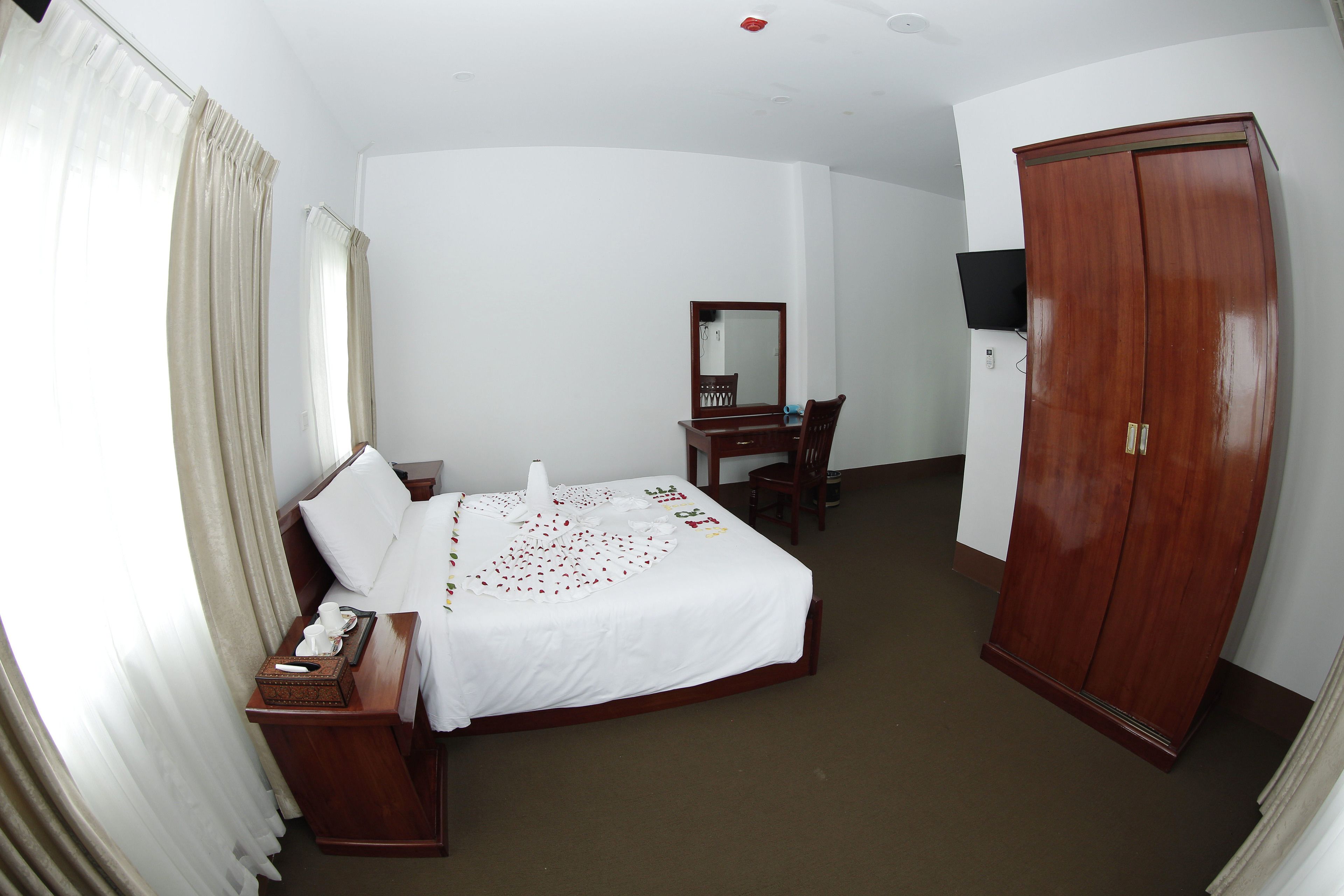 Habitación de hotel con cama, escritorio, silla, armario, televisor y ventana con cortinas.