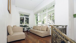 Amplia sala de estar con piso de madera, dos sofás color beige y una escalera con barandilla ornamentada.