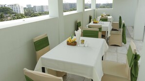 Un comedor con mesas dispuestas para el servicio, sillas con cintas verdes y vistas a edificios al fondo.