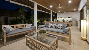 Un amplio espacio al aire libre con dos sofás de madera, una mesa de centro de vidrio y un ventilador de techo.