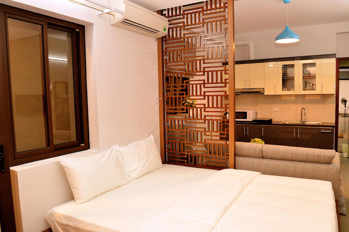 Une chambre avec un lit, une cloison en bois, un coin cuisine et une salle de bain visible à travers une porte ouverte.