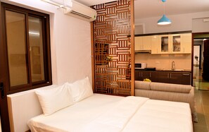 Un dormitorio con cama, un separador de madera, una kitchenette y un baño visible a través de una puerta abierta.