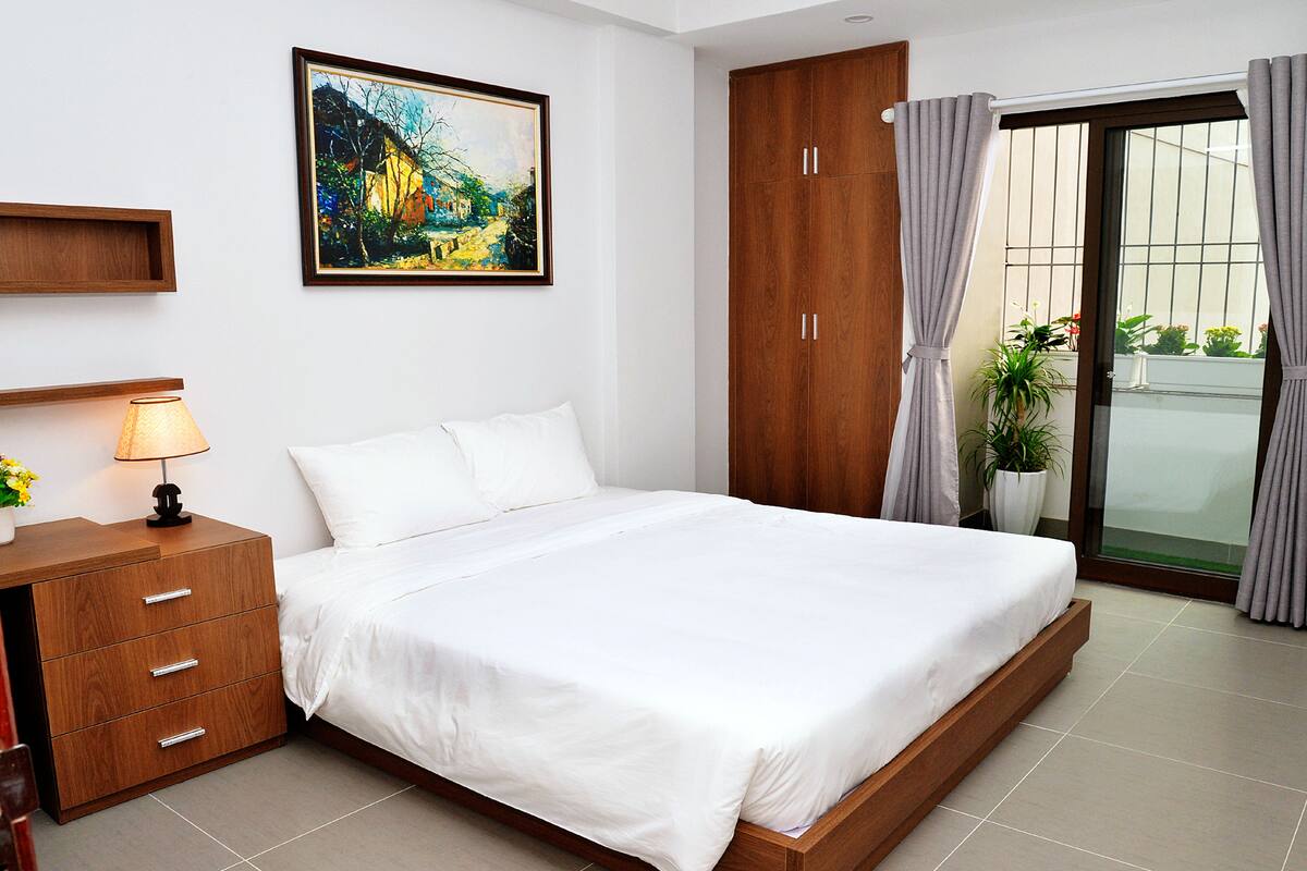 Une chambre bien rangée, avec un lit, une table de chevet, une lampe et un tableau accroché au mur.
