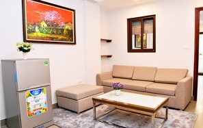 Una sala de estar con sofá, una mesa de centro, un refrigerador y un cuadro en la pared.
