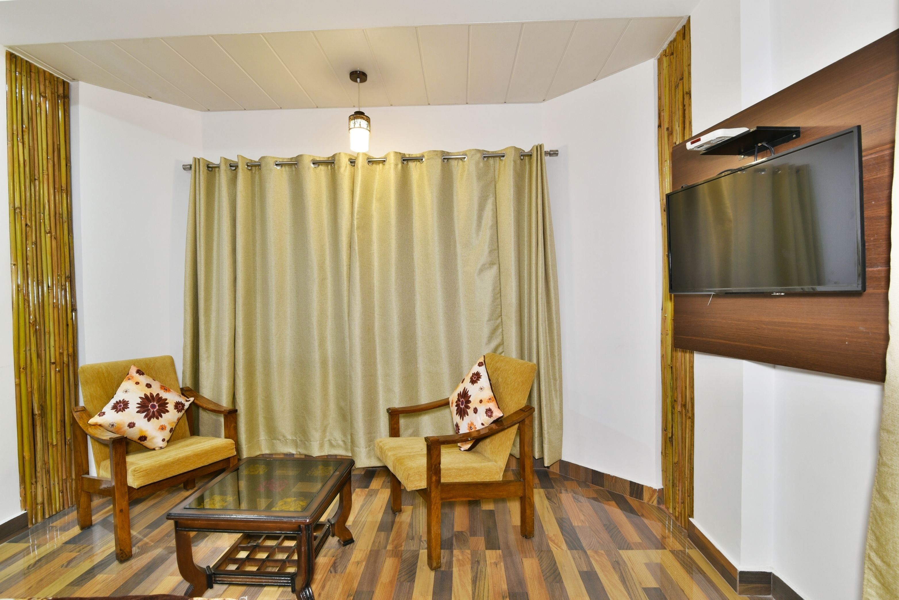 A living room with two wooden chairs, a glass coffee table, a television mounted on the wall, and a curtain.