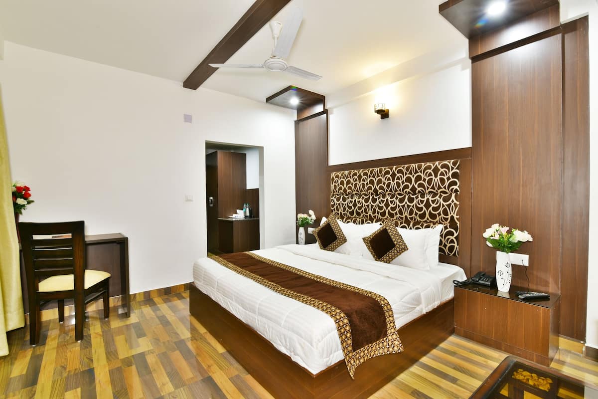 A hotel room with a large bed, a desk, a chair, a ceiling fan, and a decorative headboard.