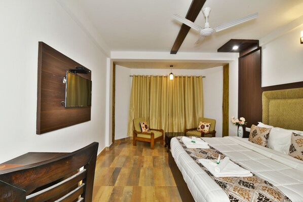 A hotel room with a bed, two chairs, a desk, a mirror, and a ceiling fan. - Kapoor Resort (Manali)