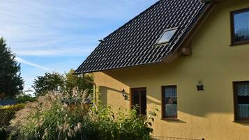Ein Haus mit Ziegeldach, einer kleinen Veranda und einem umzäunten Garten.