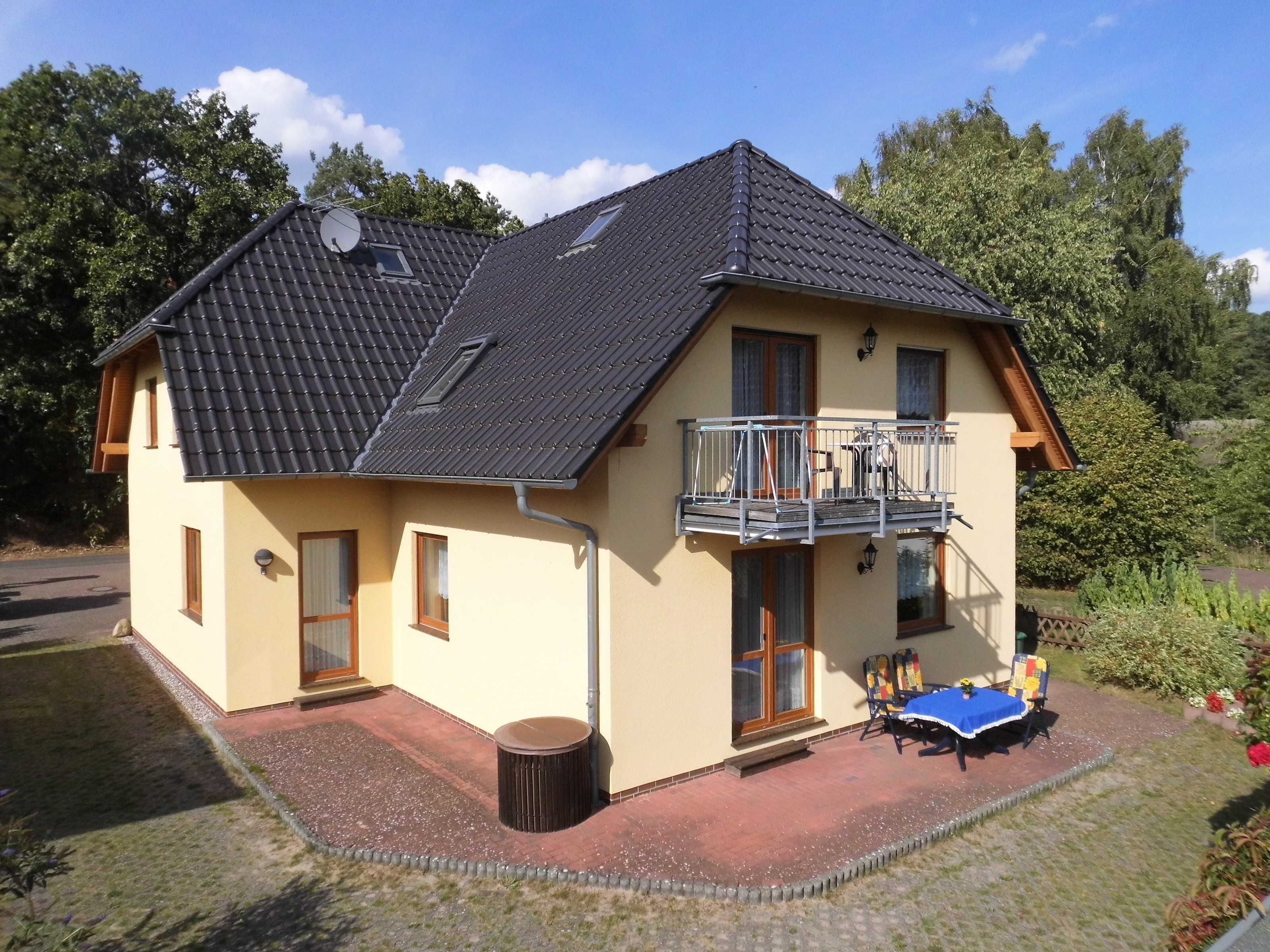 Ein zweistöckiges Haus mit Balkon, einer Terrasse mit Tisch und Stühlen sowie einem Garten.