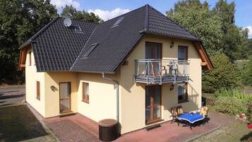 Ein zweistöckiges Haus mit Balkon, einer Terrasse mit Tisch und Stühlen sowie einem Garten.