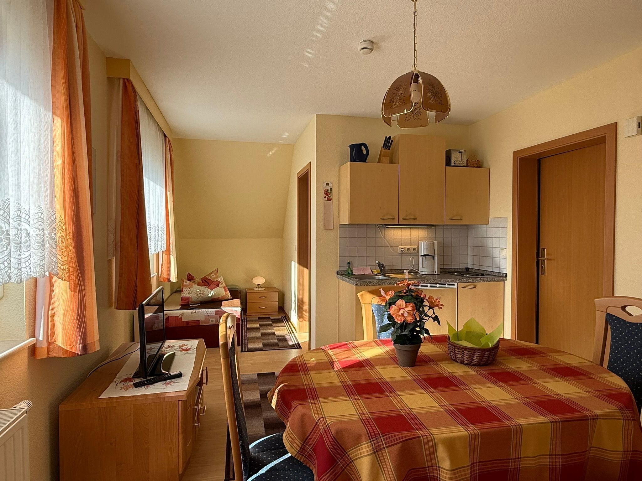 Ein kompaktes Hotelzimmer mit Küchenzeile, Essbereich und einem Bett mit Karoüberwurf.