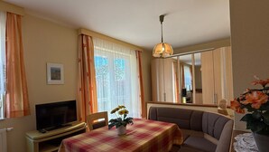 A cozy living room with a sofa, a table with a plaid tablecloth, a television, and a mirror reflecting the room.