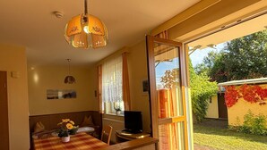 A cozy room with a wooden bench and table, a television, and a large window offering a view of a garden.