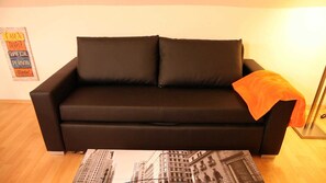 A black sofa with two cushions and an orange throw blanket. - Art City-Studio Kassel 5 - ART City-Studio Kassel 5 (Niestetal)