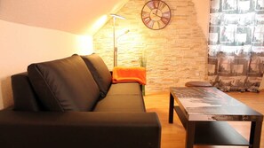 A living room with a sofa, a table, a lamp, and a clock on the wall.
