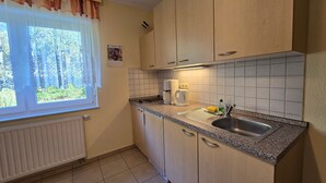 Pieni, käytännöllinen keittiö, jossa on ikkuna, pesuallas, liesi ja kaapistot.
