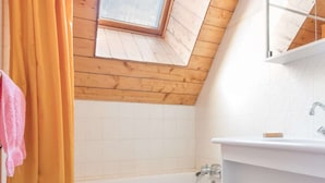A modern bathroom with a skylight, a bathtub, and a white sink.