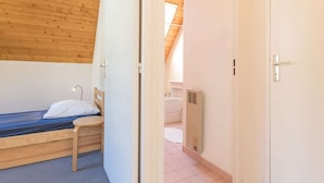 A small, single-bed room with a wooden headboard, a bedside table, and a window with a view of a bathroom.