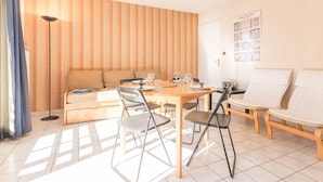 A modern living room with a wooden panel wall, a dining table with chairs, a sofa, and a ceiling light fixture.