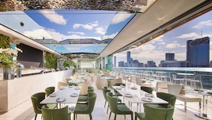 Un restaurante en la azotea con mesas al aire libre, diseño moderno y vistas al horizonte de la ciudad.
