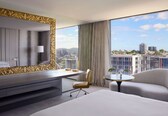A modern hotel room with a large bed, a desk, a chair, and a round table.