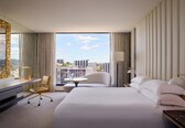 A hotel room with a large bed, a desk, a chair, and a view of the cityscape.