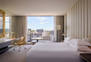 A hotel room with a large bed, a desk, a chair, and a view of the cityscape.