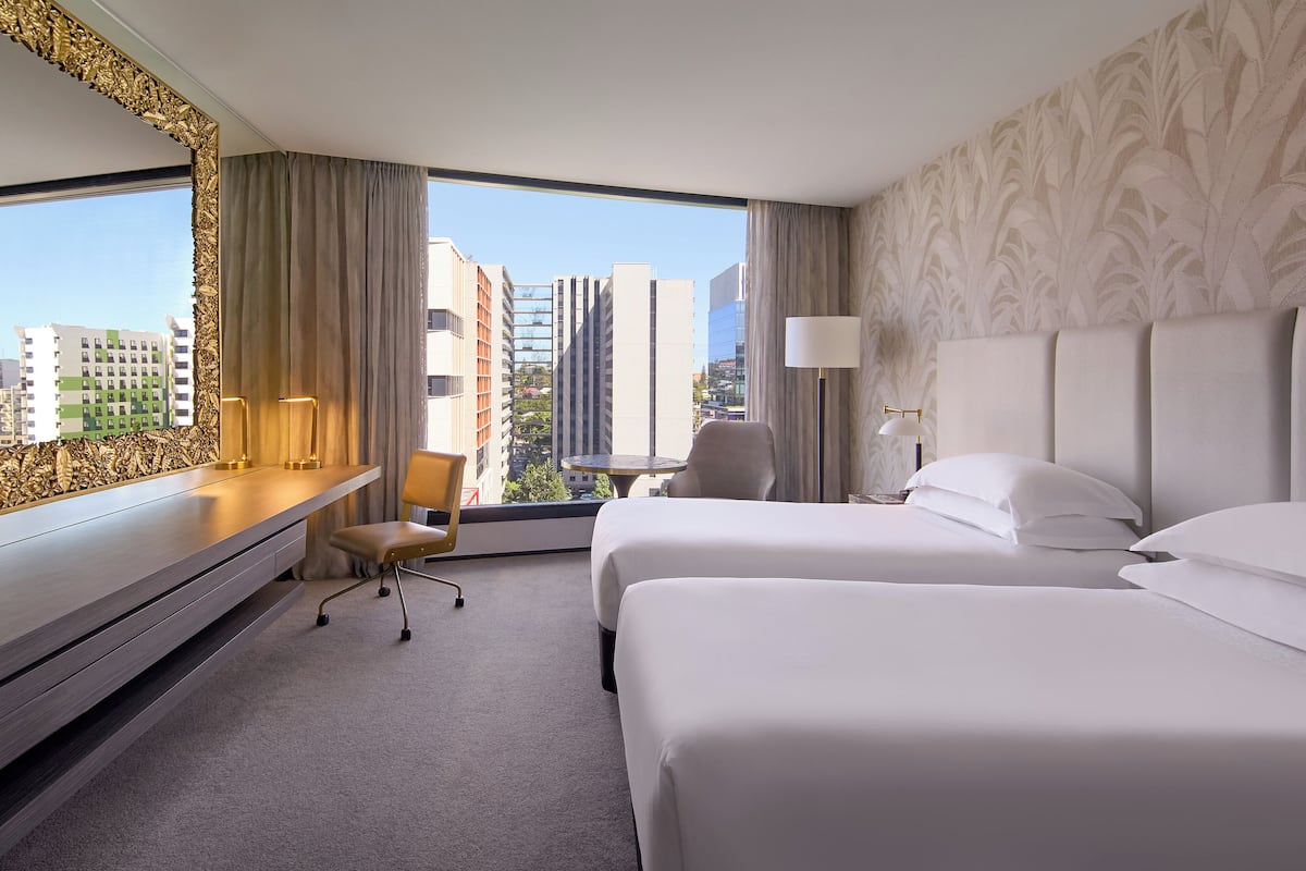 Een hotelkamer met twee bedden, een bureau met stoel, een lamp en uitzicht op de stad.