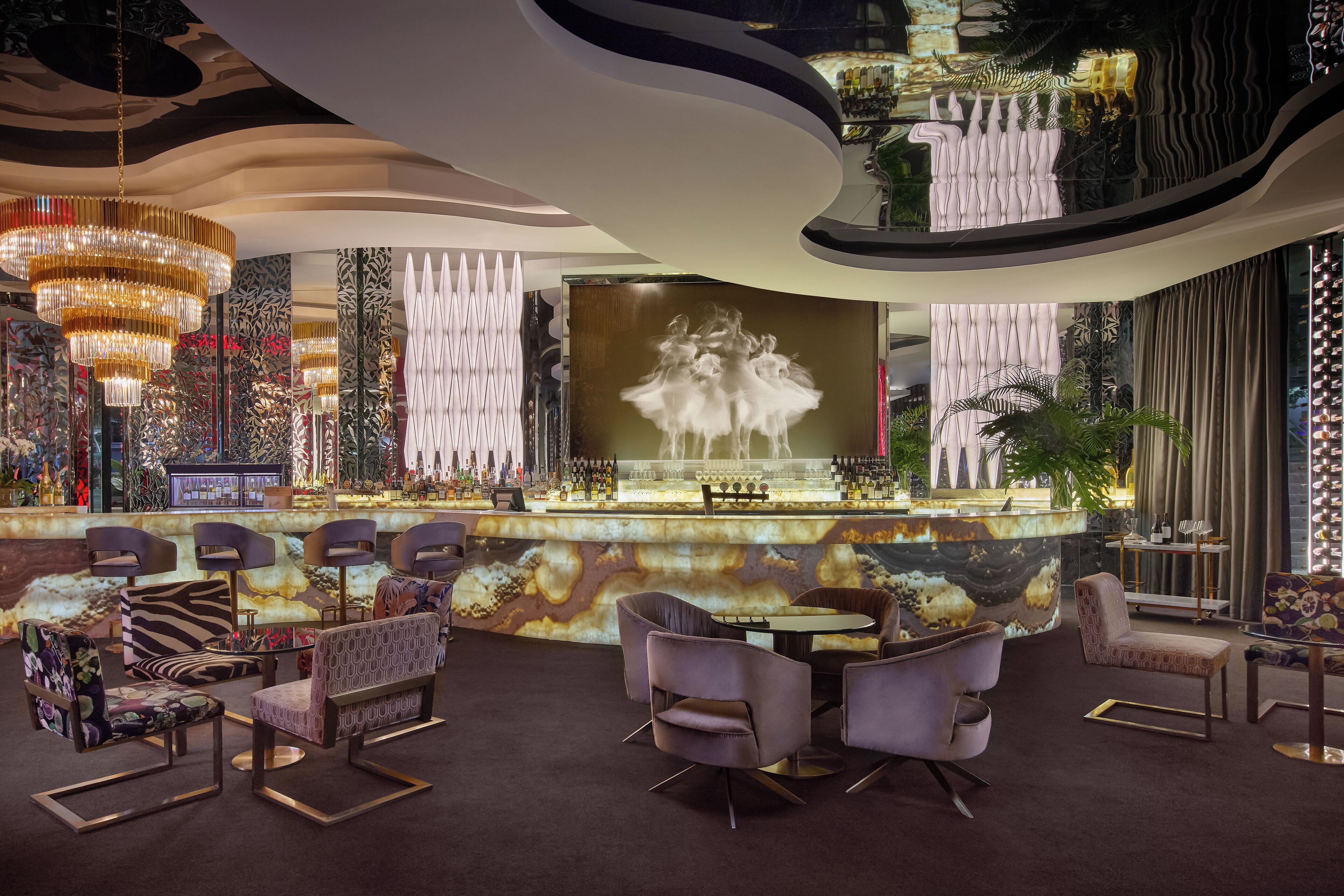 A bar area with modern seating, a large chandelier, and a decorative wall.