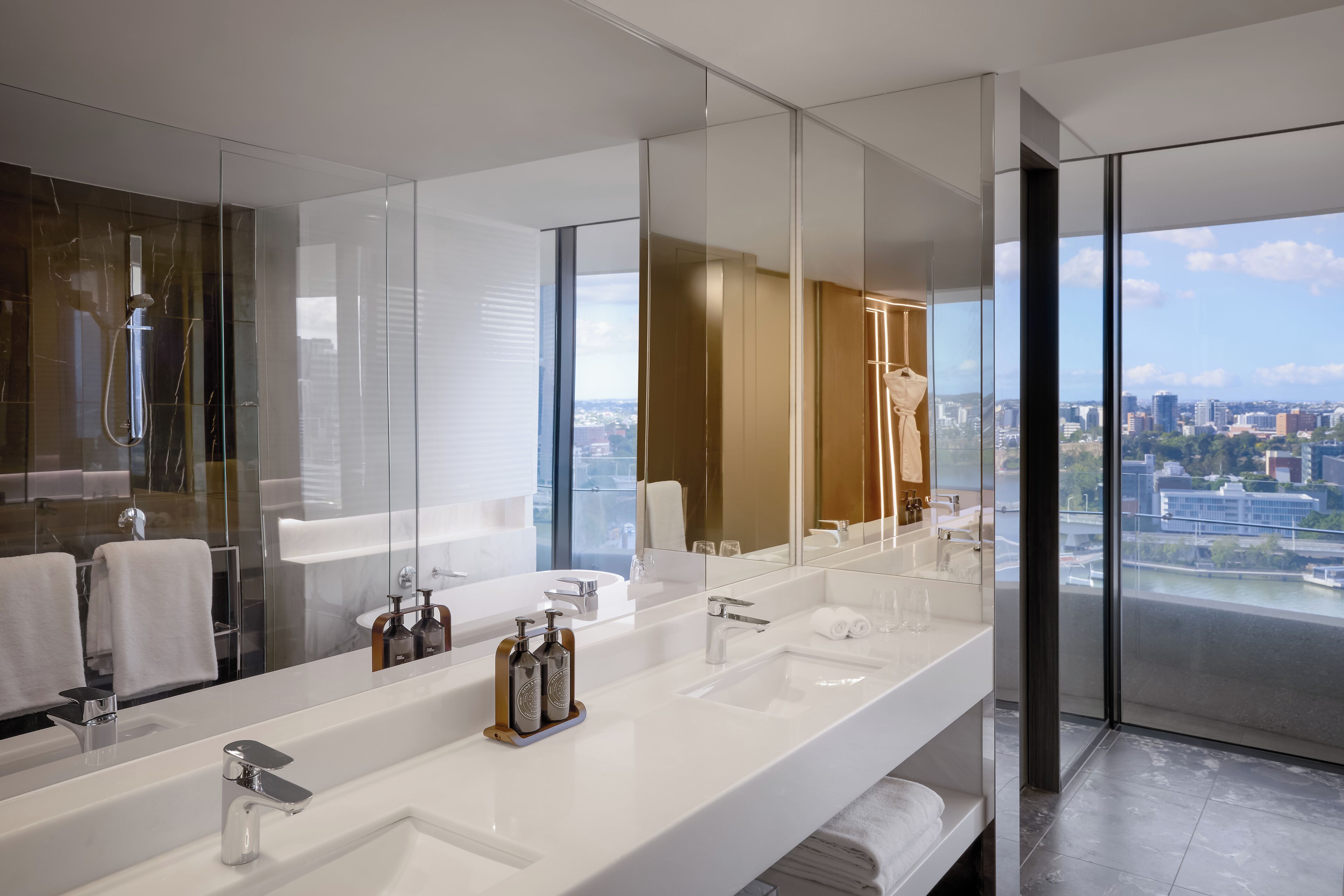 A modern bathroom with a large mirror, two sinks, and a shower.