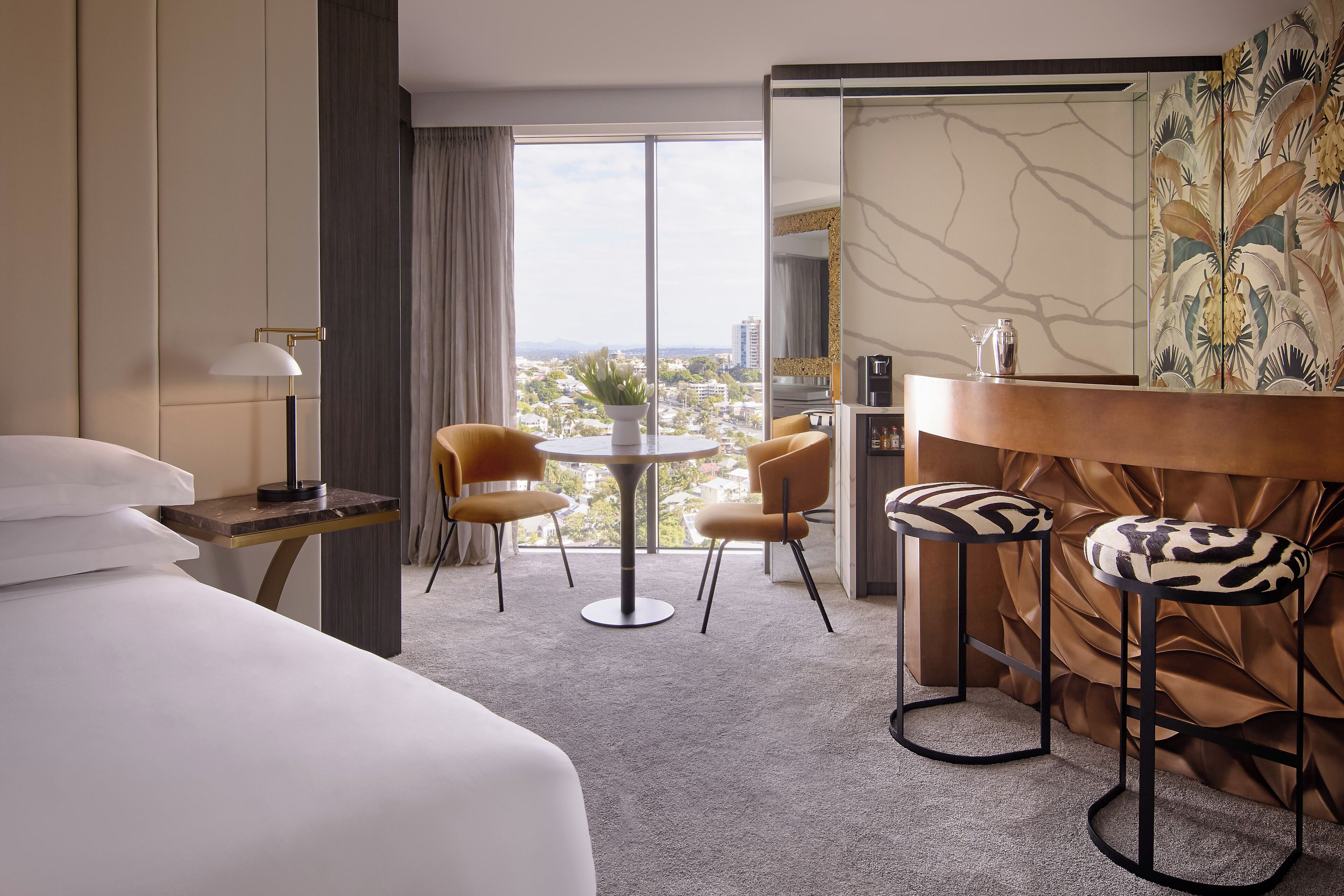 Een hotelkamer met een bed, twee stoelen, een tafeltje, een lamp en uitzicht op de stad.