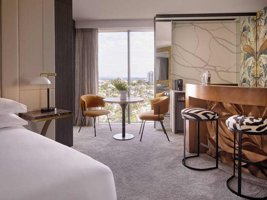 Een hotelkamer met een bed, twee stoelen, een tafeltje, een lamp en uitzicht op de stad.