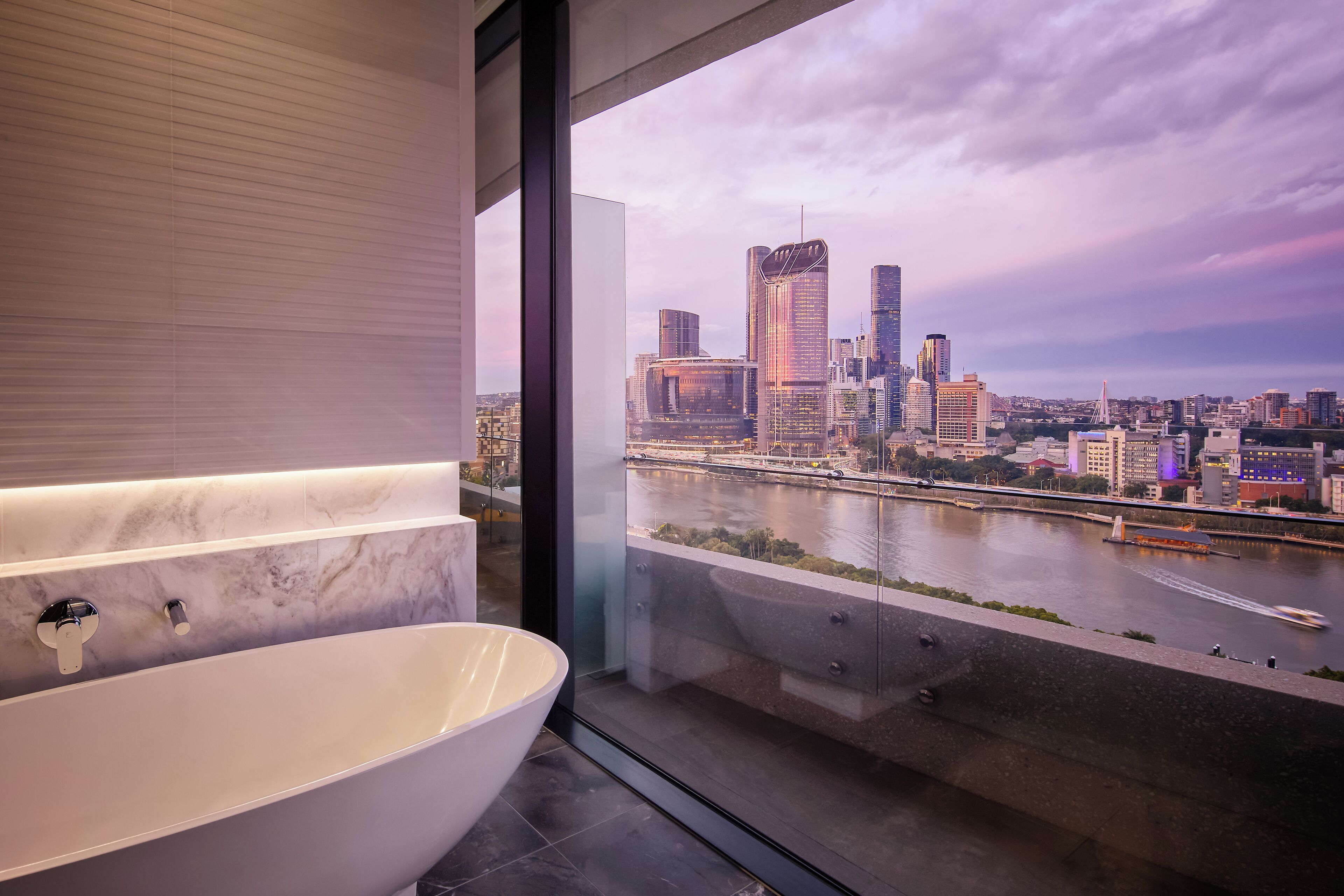 A modern bathroom with a large bathtub and a city view through a glass window.