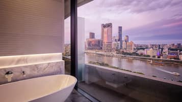 A modern bathroom with a large bathtub and a city view through a glass window.
